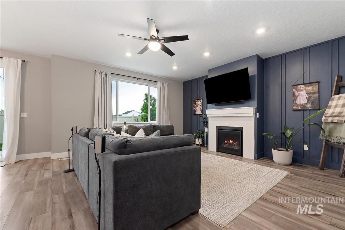 815 Knowledge Street Middleton, ID 83644 - Photo 8 of 49 Living area featuring a floor-to-ceiling fireplace with a white mantel, a dark blue accent wall with vertical paneling, wood-finish flooring, a ceiling fan with integrated lighting, and recessed ceiling lights