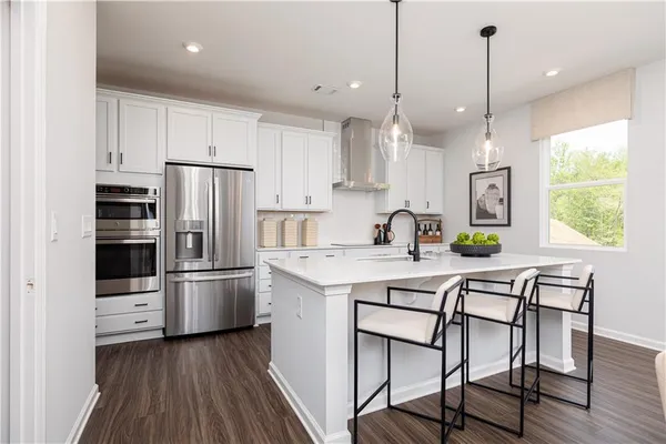 a kitchen with stainless steel appliances a stove a sink a refrigerator and white cabinets with wooden floor