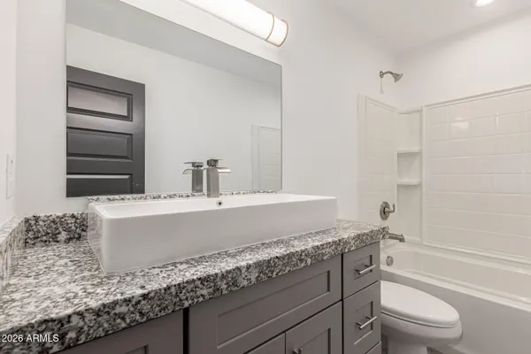 a bathroom with a granite countertop bathtub shower sink vanity and toilet