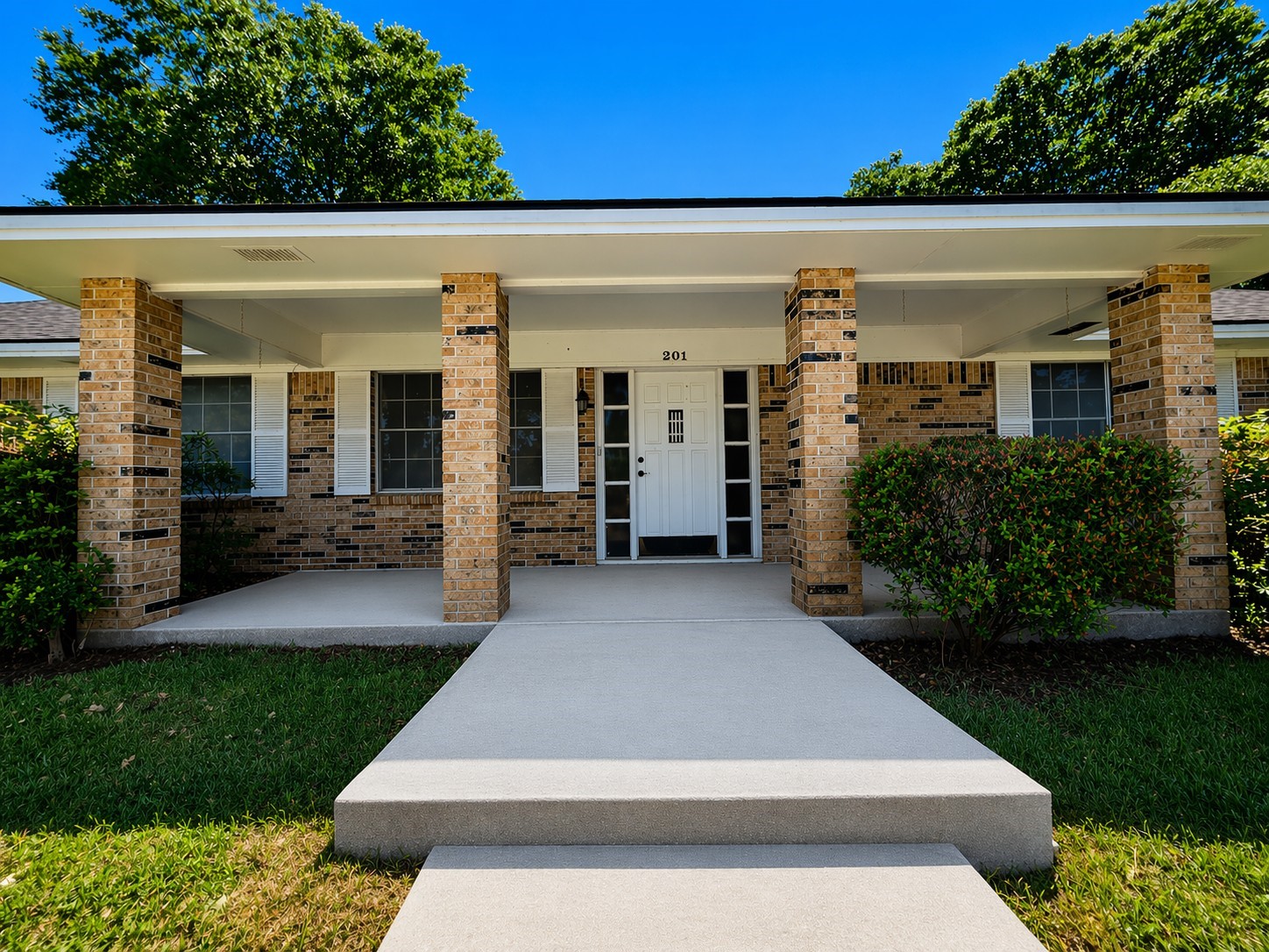 Charming single-story home with a welcoming front porch, brick exterior, and neatly landscaped yard. Large windows provide ample natural light.