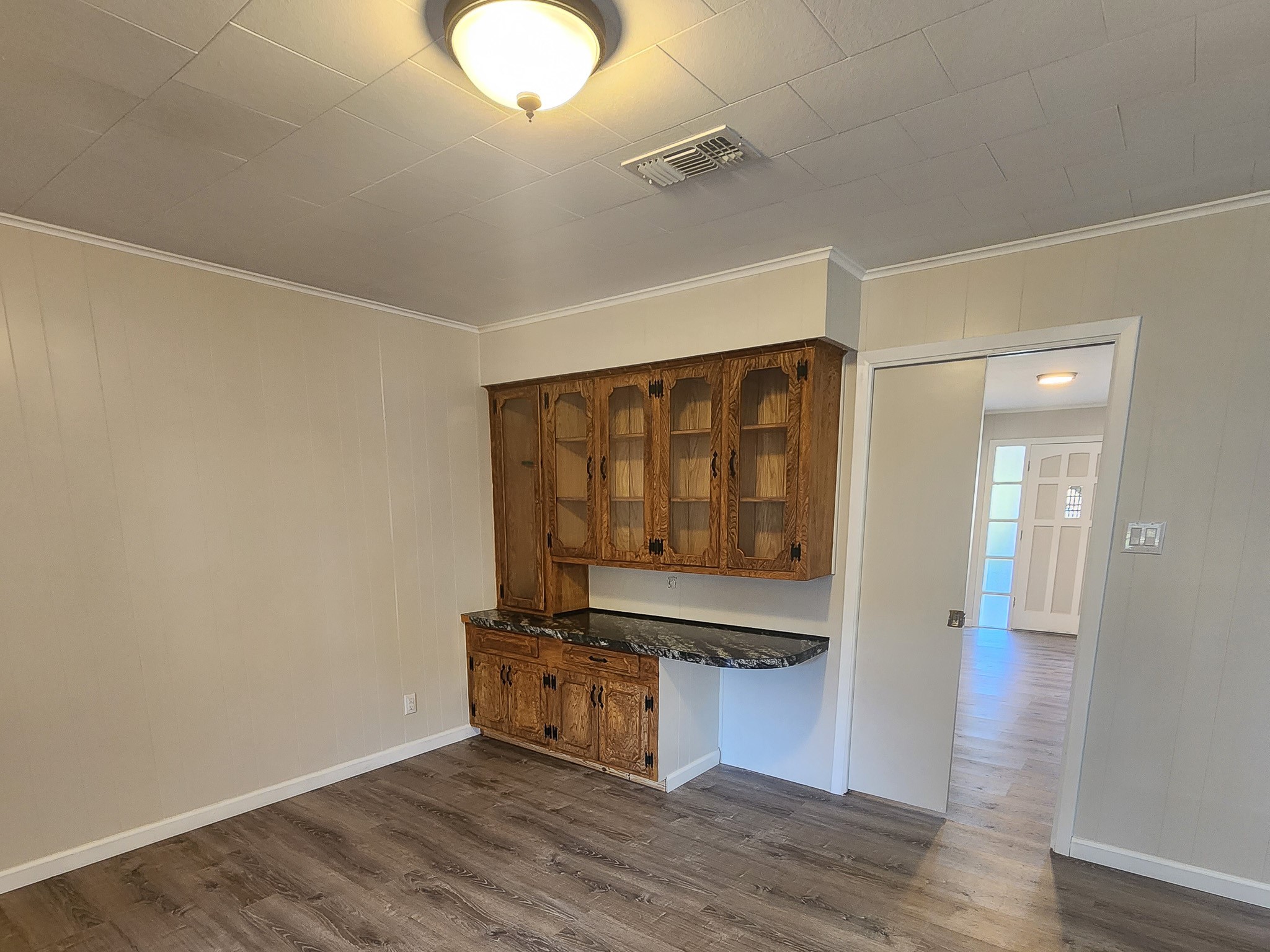 201 Verna Street Jasper, TX 75951 - Photo 13 of 27 This room features wood-paneled walls and flooring, a built-in wooden cabinet with glass doors, and a ceiling light fixture. The space opens to another room through a sliding door, offering a cozy and functional layout.