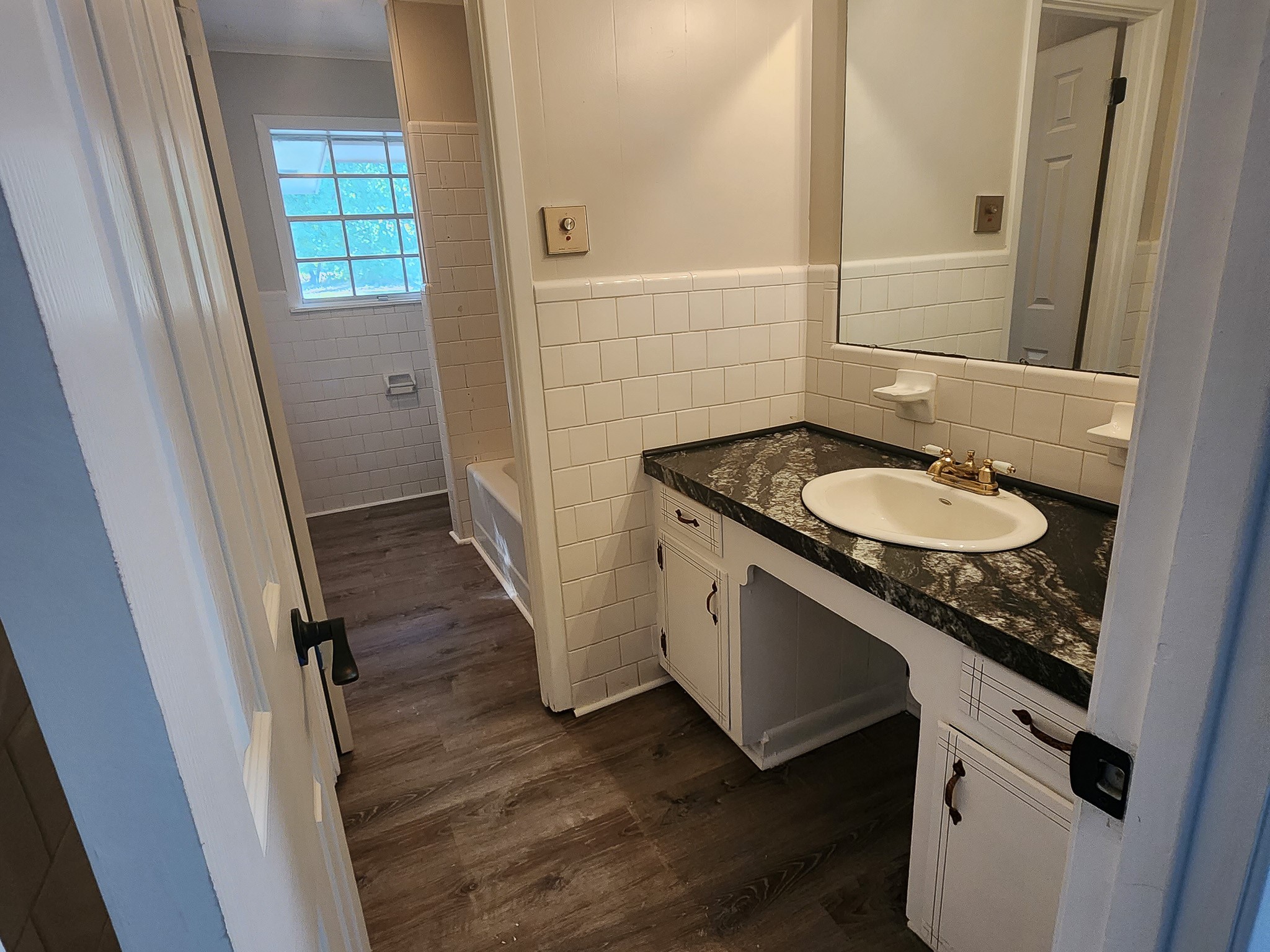 201 Verna Street Jasper, TX 75951 - Photo 18 of 27 This bathroom features a sleek black countertop with a white sink, surrounded by classic white tile backsplash. It includes a bathtub and has wood-style flooring, creating a clean and inviting space.