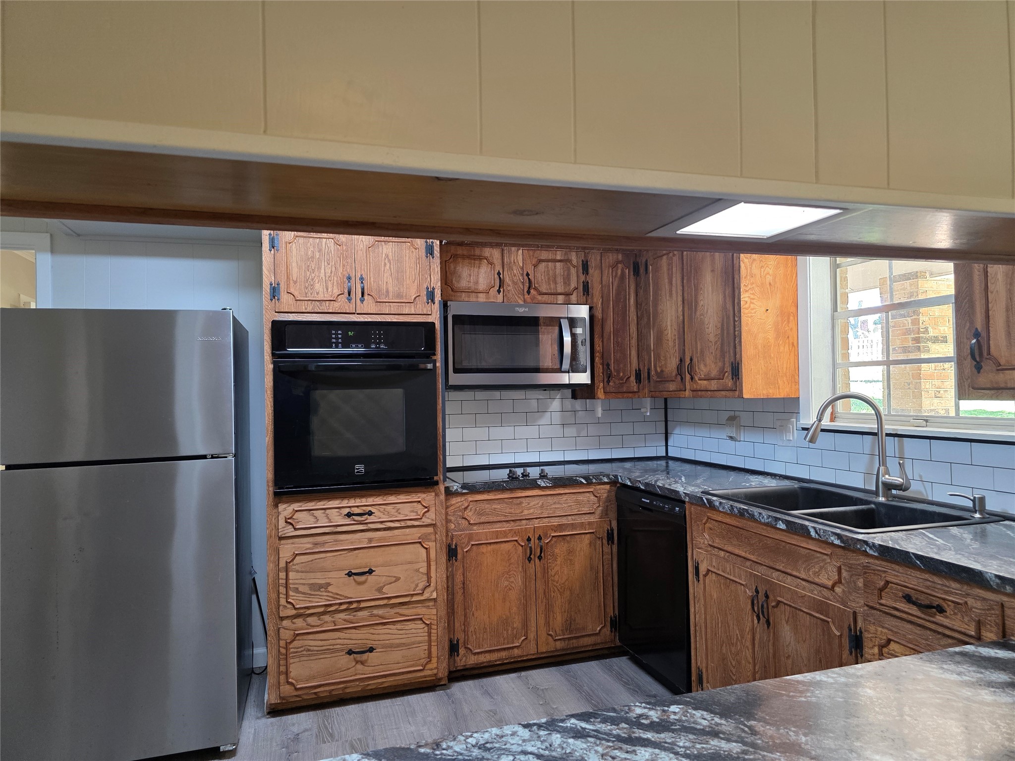 201 Verna Street Jasper, TX 75951 - Photo 2 of 27 This kitchen features rustic wooden cabinetry, stainless steel appliances, and a sleek black countertop. The white subway tile backsplash and ample natural light from the window add a modern touch.