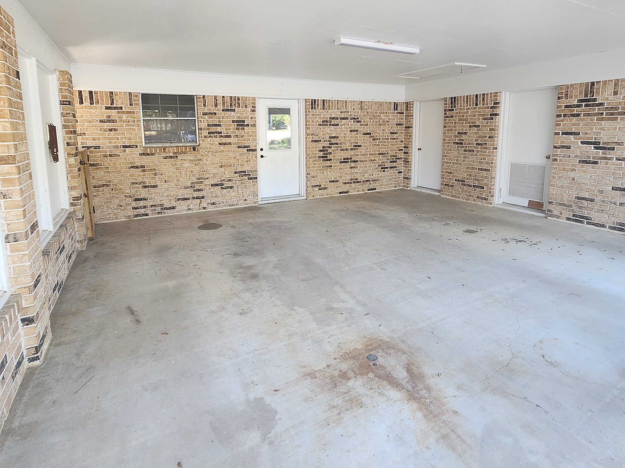 201 Verna Street Jasper, TX 75951 - Photo 22 of 27 A spacious, enclosed garage with brick walls, a concrete floor, and a white door leading outside, offering ample room for parking or storage.