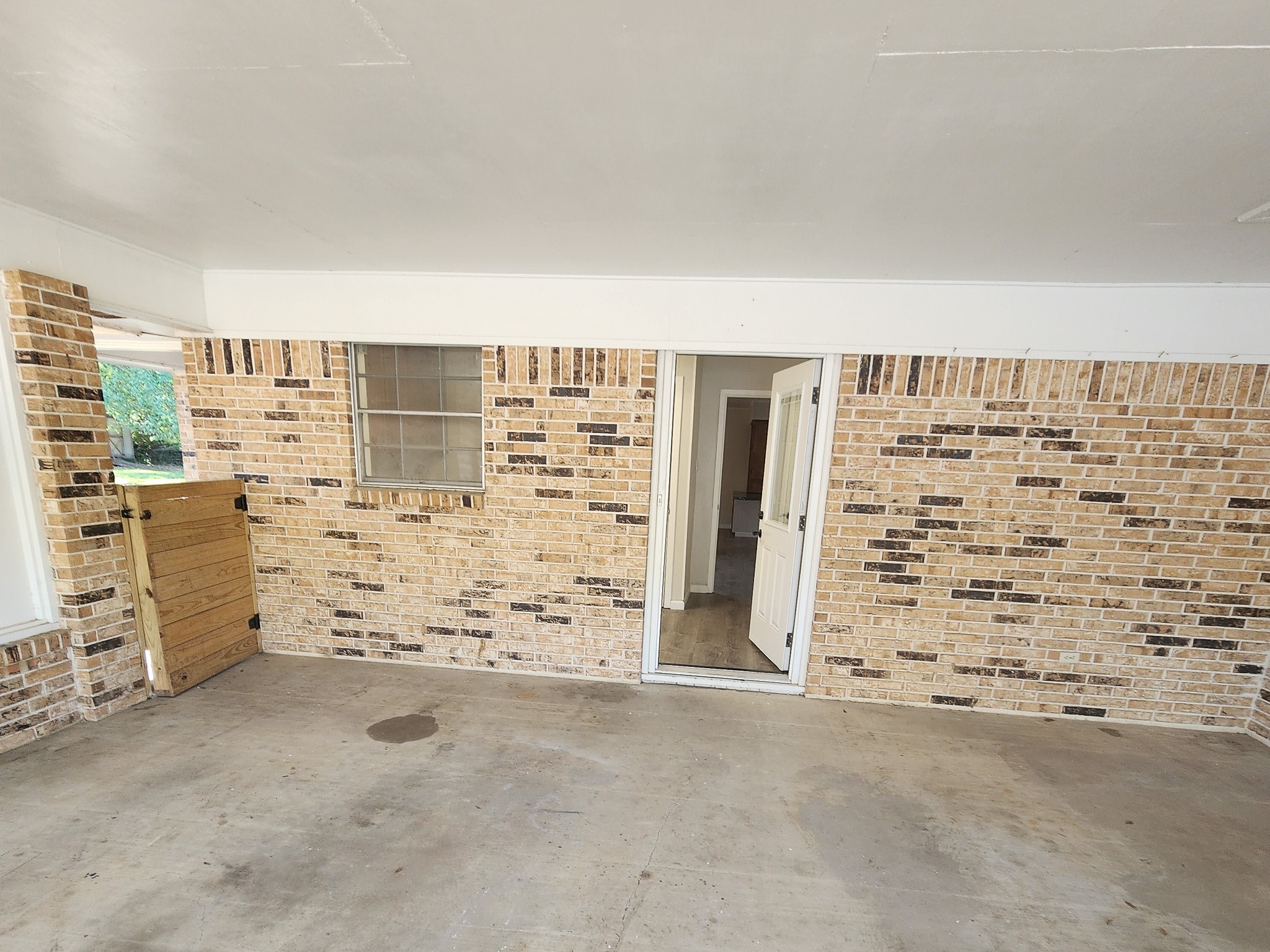 201 Verna Street Jasper, TX 75951 - Photo 23 of 27 This photo shows a partially enclosed patio or porch area featuring brick walls and a concrete floor. It includes a window and a doorway leading inside, offering potential for an outdoor living space or entryway.