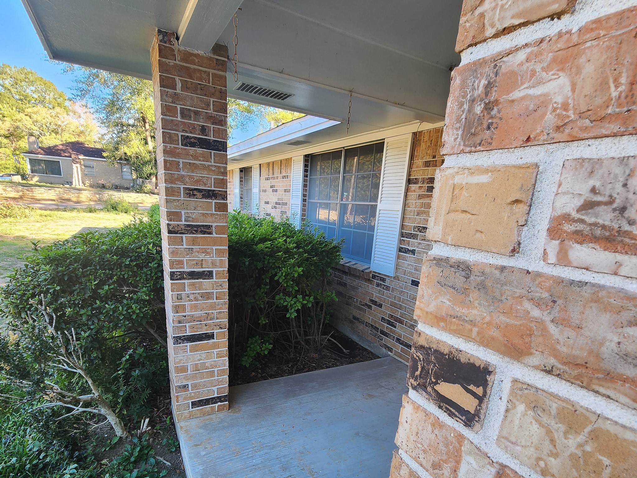201 Verna Street Jasper, TX 75951 - Photo 24 of 27 This photo showcases a cozy brick porch with a covered entryway, featuring a well-maintained garden and a large window with shutters, perfect for enjoying the outdoors in a quiet neighborhood setting.