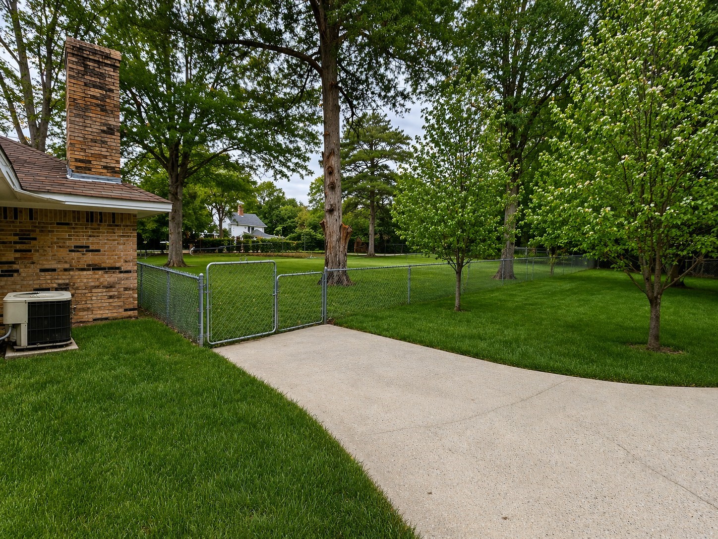 201 Verna Street Jasper, TX 75951 - Photo 26 of 27 Spacious backyard with lush green grass and mature trees, featuring a brick exterior, chain-link fencing, and a paved patio area. Ideal for outdoor activities and relaxation.