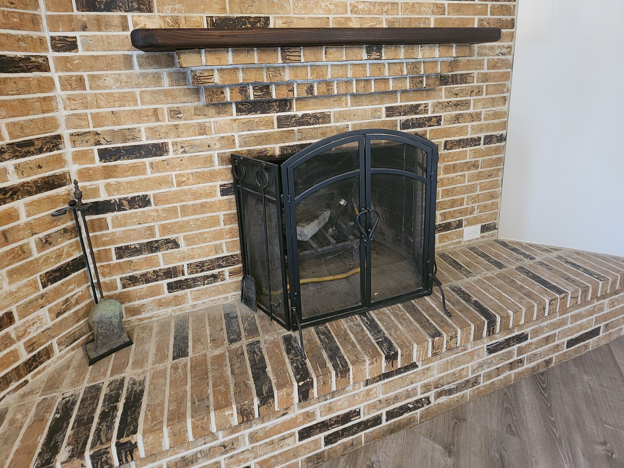 201 Verna Street Jasper, TX 75951 - Photo 4 of 27 Showcases a rustic brick fireplace with a sturdy metal screen, wooden mantel, and a hearth extending outward. The surrounding area features wood-look flooring, adding warmth and charm to the living space.