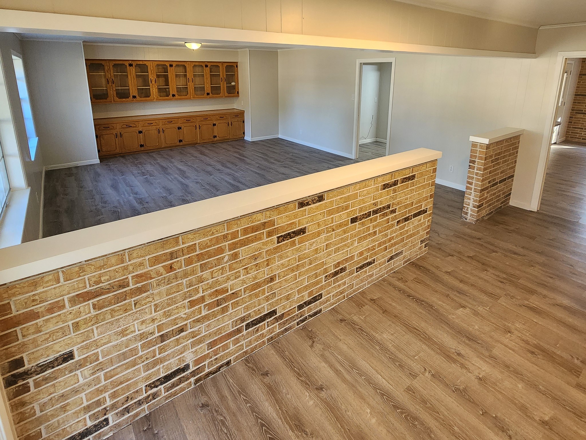 201 Verna Street Jasper, TX 75951 - Photo 6 of 27 This spacious room features stylish flooring and a brick half-wall, providing a cozy and open layout. Built-in wooden cabinetry adds ample storage and character to the space.
