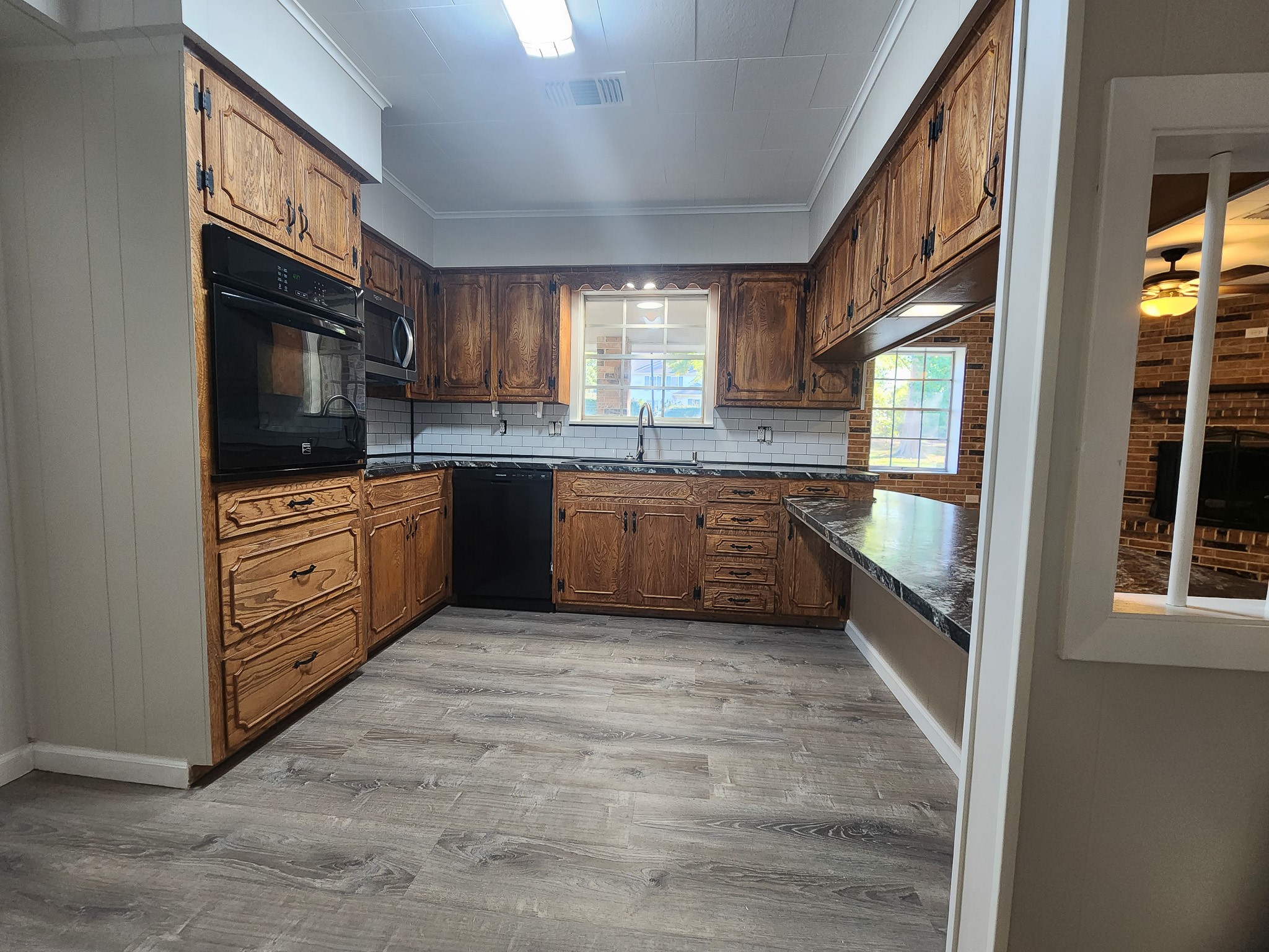 201 Verna Street Jasper, TX 75951 - Photo 10 of 27 This kitchen features rustic wooden cabinets, modern appliances, and a stylish tile backsplash. The open layout includes a large window for natural light and a serving counter that connects to the living area with a cozy fireplace.