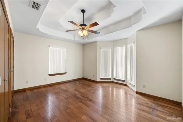 an empty room with wooden floor chandelier fan and windows