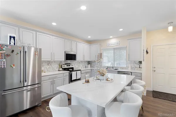 a kitchen with stainless steel appliances granite countertop a refrigerator a stove a sink a dining table and chairs