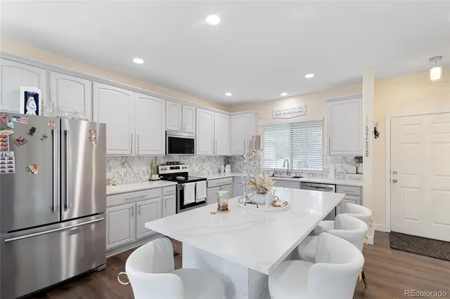 a kitchen with stainless steel appliances granite countertop a refrigerator a stove a sink a dining table and chairs