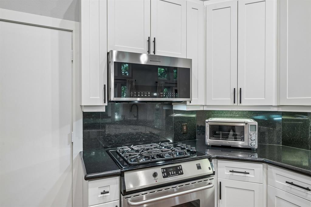 3553 Wheeler Street Dallas, TX 75209 - Photo 15 of 35 Gas range and stainless steel microwave detail with black granite backsplash and white shaker cabinets