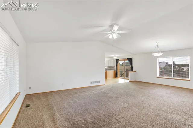 an empty room with chandelier fan and windows