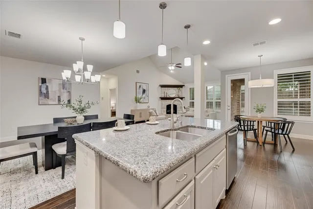 a kitchen with granite countertop kitchen island stainless steel appliances a table chairs sink and wooden floor