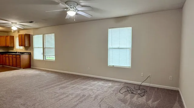 an empty room with chandelier fan and windows
