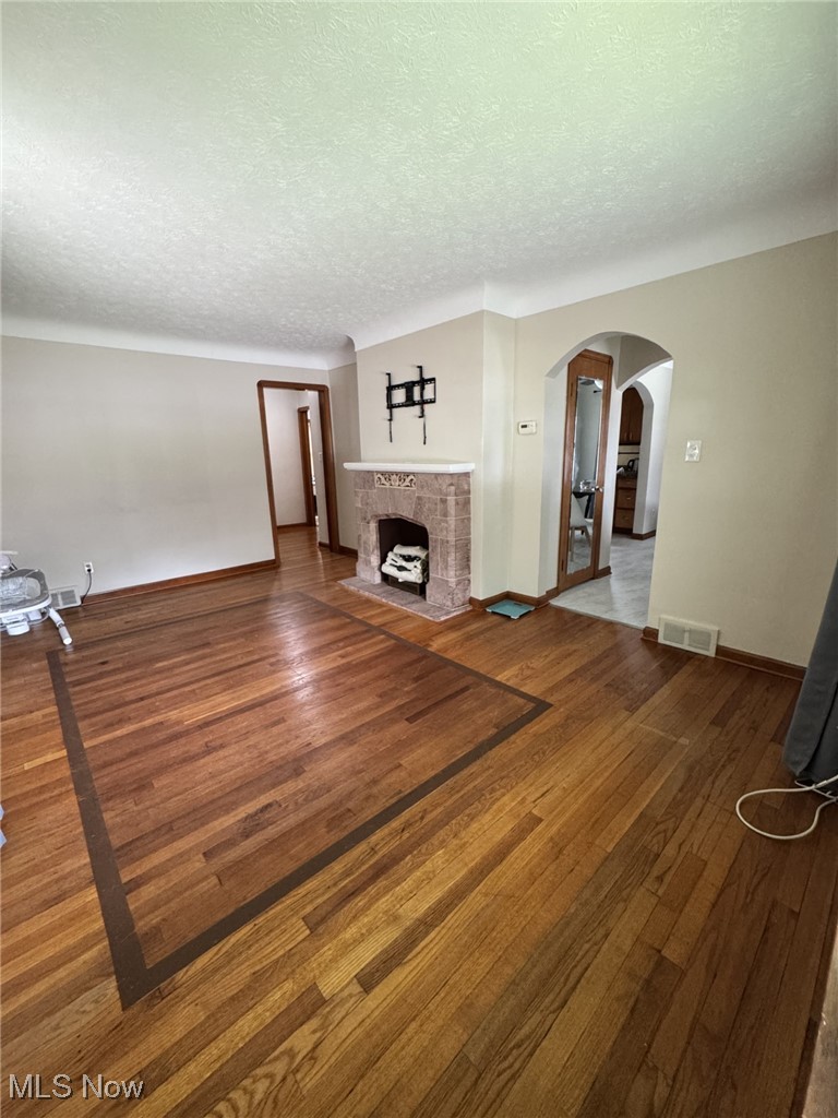 3712 Snow Road Cleveland, OH 44134 - Photo 14 of 40 Unfurnished living room featuring a textured ceiling, wood finished floors, a tiled fireplace, and arched walkways