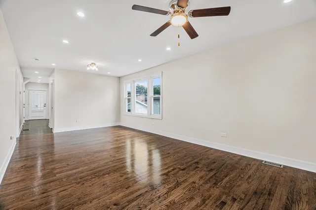 an empty room with wooden floor chandelier fan and windows