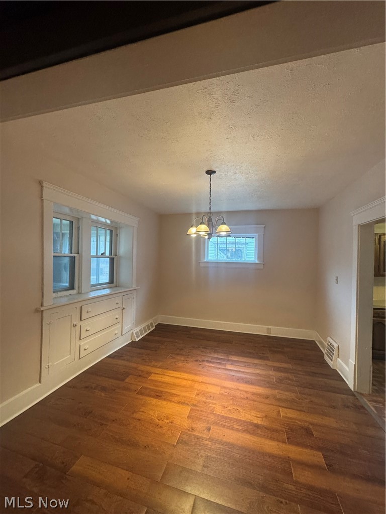 577 Rhodes Avenue Akron, OH 44307 - Photo 6 of 19 Unfurnished dining area featuring a textured ceiling, dark wood-style floors, hanging lights, and healthy amount of natural light