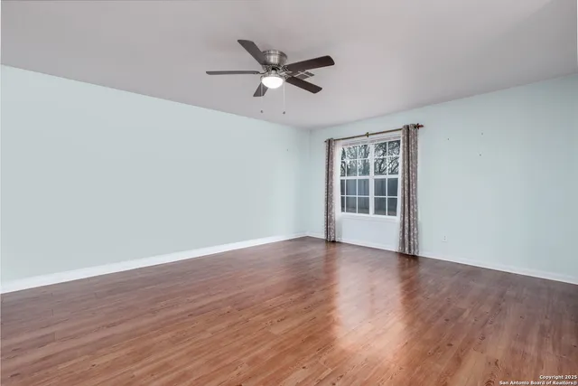 a view of an empty room with wooden floor and a ceiling fan