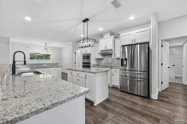 a kitchen with stainless steel appliances granite countertop a refrigerator a sink a stove a dining table and chairs