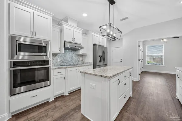 a kitchen with stainless steel appliances granite countertop a stove top oven a sink dishwasher and a microwave oven with wooden floor