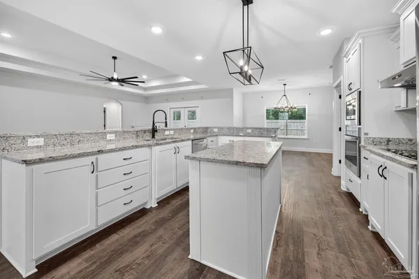 a kitchen with stainless steel appliances kitchen island granite countertop a stove a sink and white cabinets with wooden floor