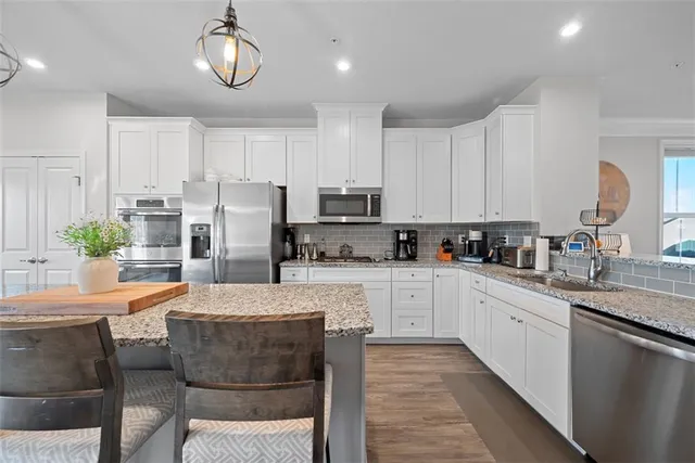 a kitchen with stainless steel appliances kitchen island granite countertop a sink a stove a refrigerator cabinets and chairs