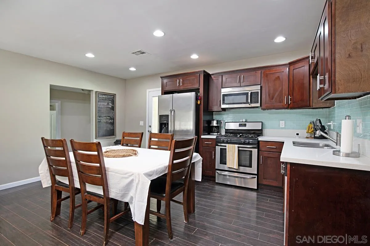 10390 Del Rio Road Spring Valley, CA 91978 - Photo 9 of 38 a kitchen with stainless steel appliances granite countertop a stove top oven a sink a dining table and chairs