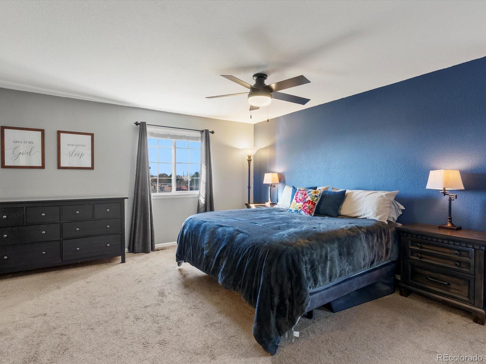 9657 Ironton Street Commerce City, CO 80022 - Photo 23 of 48 a spacious bedroom with a bed a lamp and a chandelier