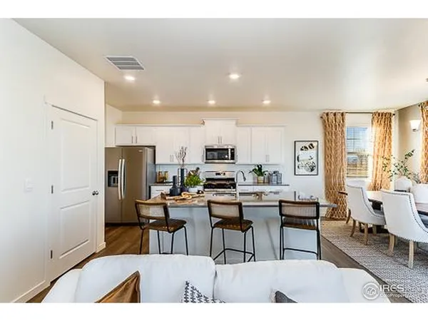 a open kitchen with stainless steel appliances kitchen island granite countertop a dining table chairs and a refrigerator