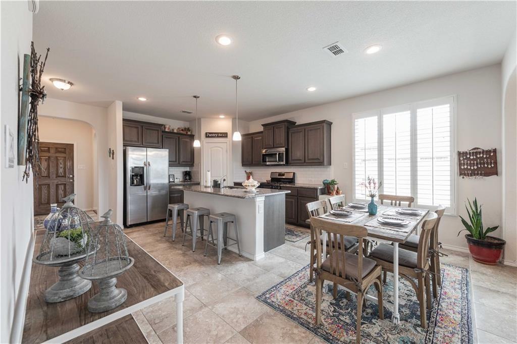 1716 Rio Penasco Road Fort Worth, TX 76052 - Photo 10 of 31 Open-concept kitchen and dining area featuring dark cabinetry, stainless steel appliances, a large central island with seating, tile flooring, recessed lighting, and abundant natural light from French doors opening to the exterior