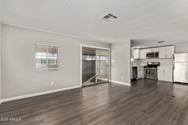 an empty room with wooden floor kitchen view and windows