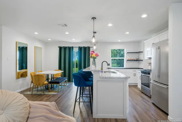 a kitchen with stainless steel appliances kitchen island granite countertop a table chairs and a refrigerator