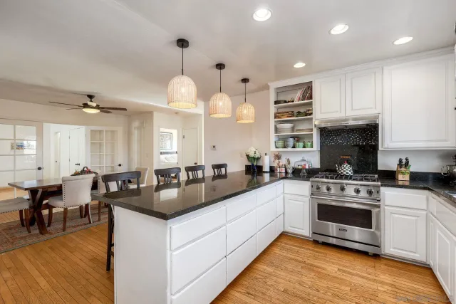 a kitchen with granite countertop a stove a sink a refrigerator and white cabinets with wooden floor