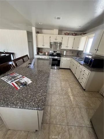 a large kitchen with kitchen island granite countertop a stove a sink a counter space and cabinets