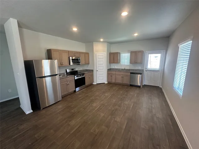 a large kitchen with a large refrigerator a sink dishwasher a stove and white cabinets with wooden floor