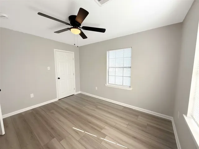 an empty room with wooden floor ceiling fan and window