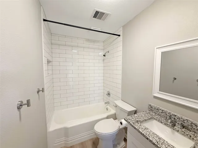 a bathroom with a granite countertop bathtub shower sink vanity and toilet