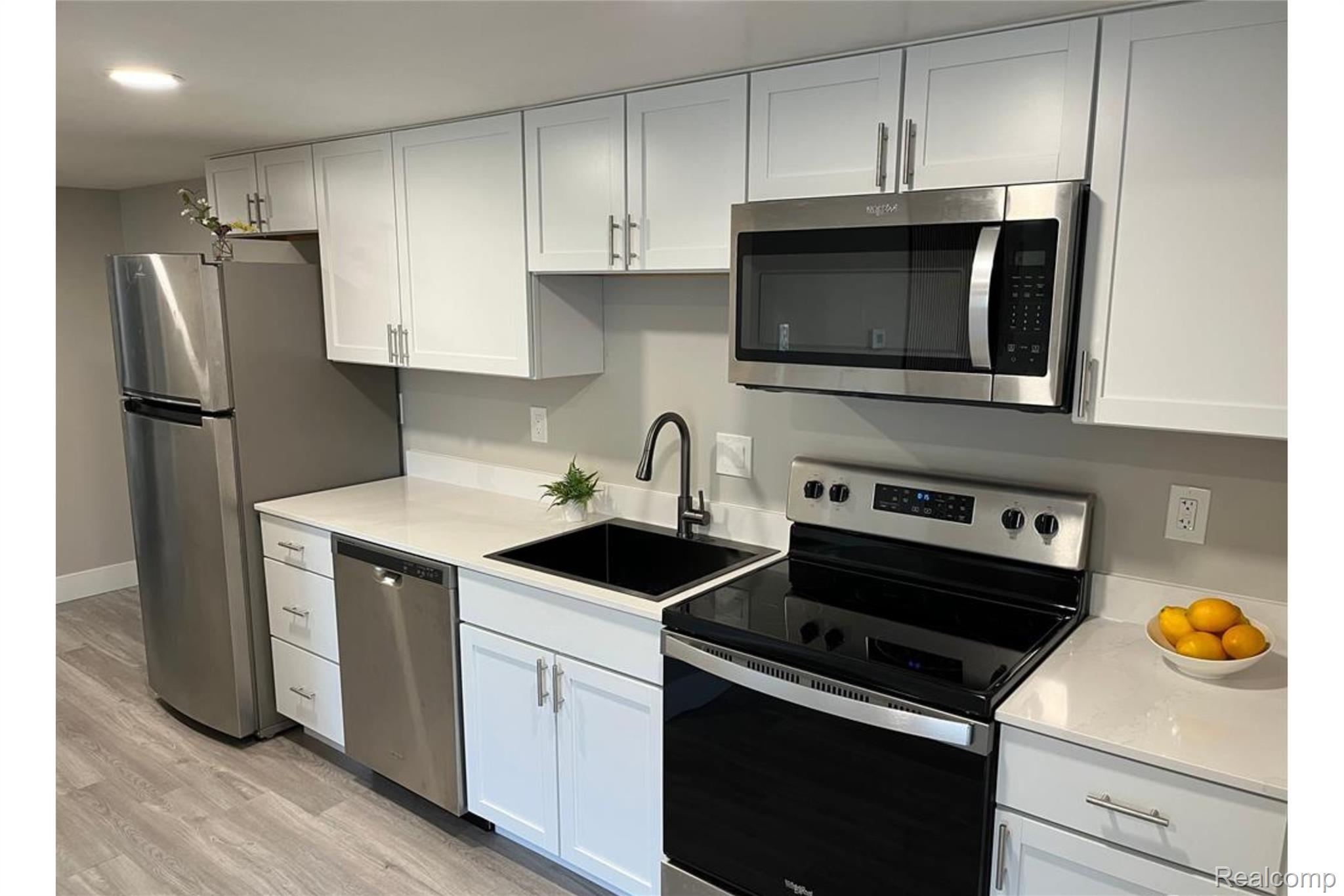 White cabinetry with silver-tone hardware, stainless steel appliances, light-toned countertops, a black sink, and wood-finish flooring