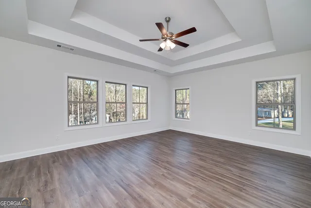 a view of an empty room with wooden floor and a ceiling fan