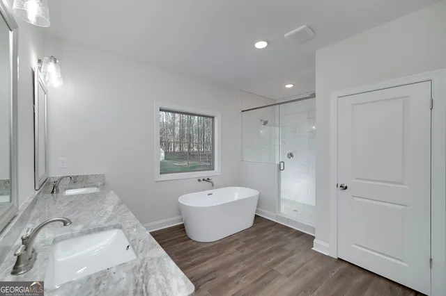 a bathroom with a granite countertop tub a double vanity sink a mirror and a large window