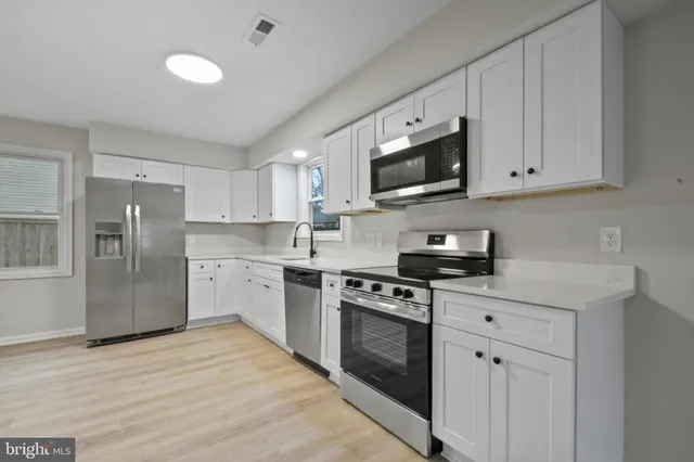 a kitchen with stainless steel appliances granite countertop white cabinets a sink a stove a refrigerator and a microwave