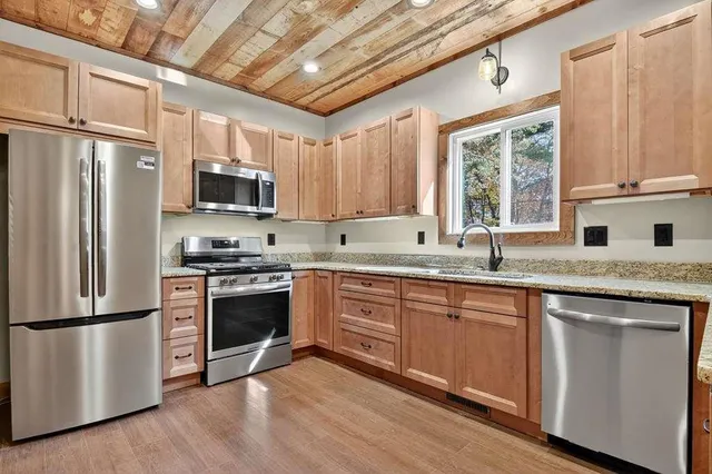 a kitchen with stainless steel appliances granite countertop a stove a sink dishwasher a refrigerator and a microwave oven with wooden floor