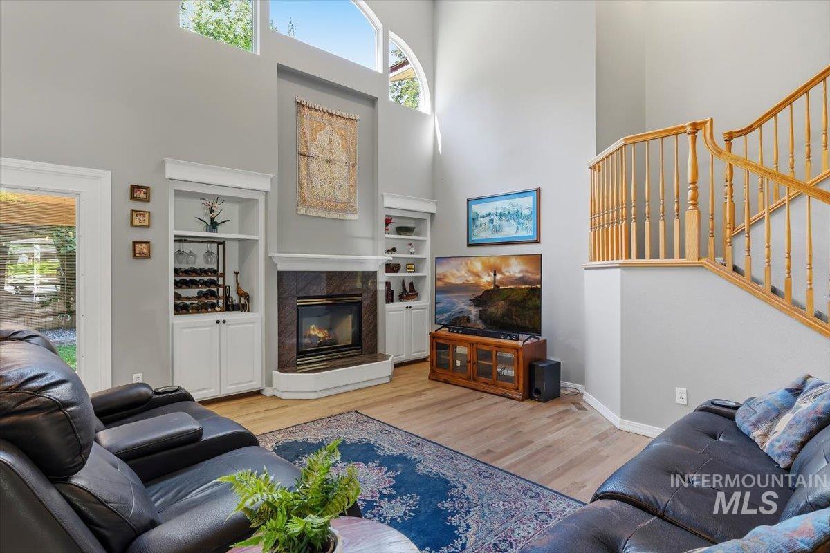 8001 West Innsbrook Court Boise, ID 83704 - Photo 11 of 39 Vaulted ceiling living area featuring a corner fireplace with stone surround, built-in shelving, wood-finish flooring, and a natural wood staircase with balusters