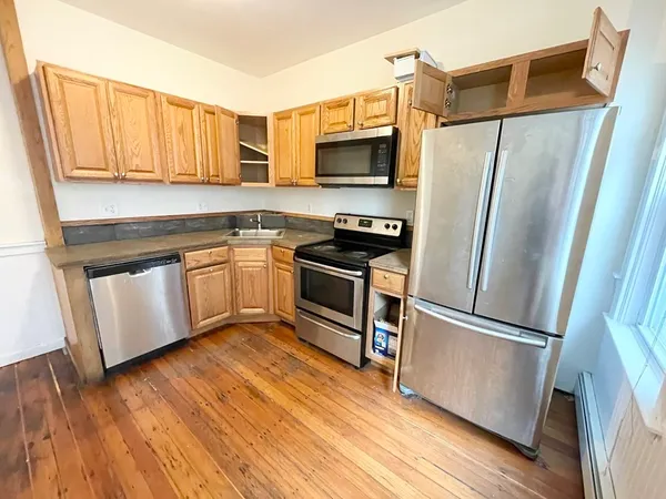 a kitchen with granite countertop a refrigerator a sink dishwasher a stove and white cabinets with wooden floor
