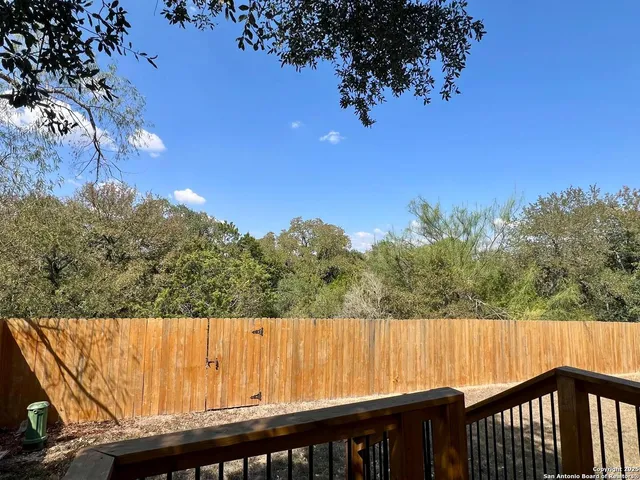 a view of a backyard with wooden fence and large trees