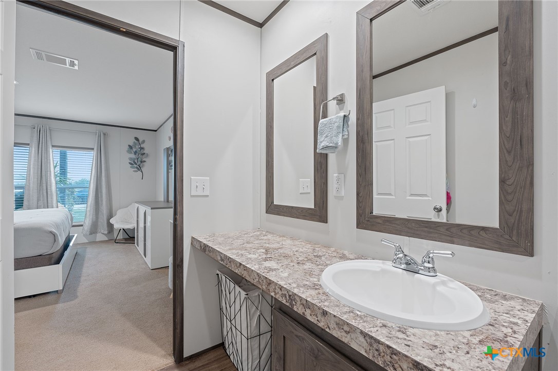 121 Fate Court Kyle, TX 78640 - Photo 19 of 23 a en suite bathroom with a granite countertop sink and a mirror