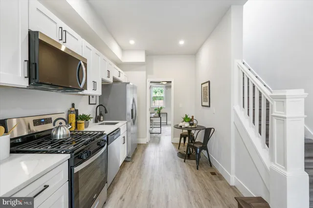 a kitchen with stainless steel appliances a stove a sink a refrigerator white cabinets and wooden floor